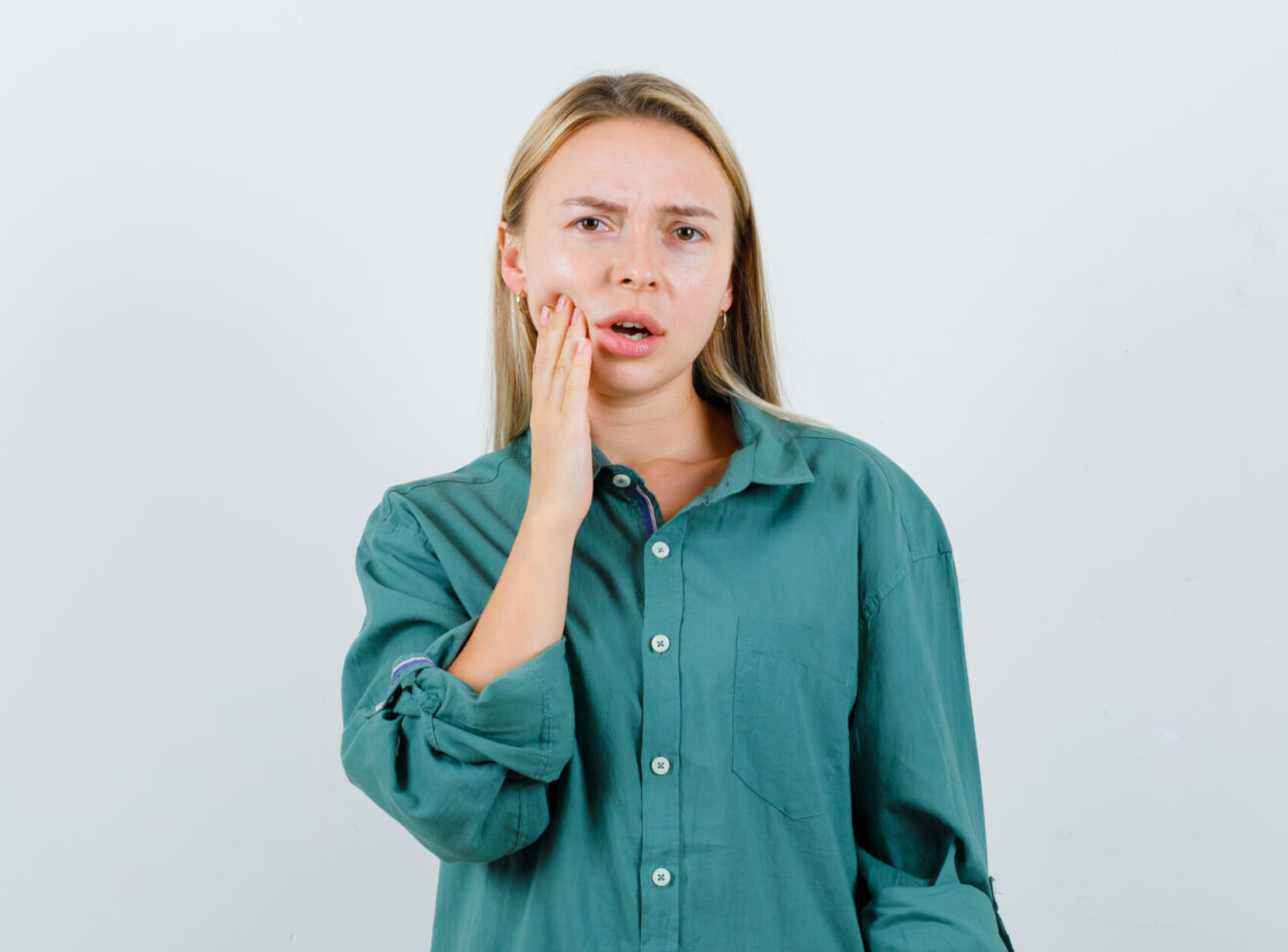 blonde woman suffering from toothache in green shirt and looking uncomfortable , front view 